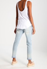 Top blanco sin mangas con espalda redondeada, jeans ajustados de color azul claro con dobladillos deshilachados y zapatillas beige con cordones. Conjunto simple y casual.