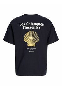T-shirt noir avec texte blanc « Les Calanques Marseilles » au-dessus d’un grand graphique jaune représentant un coquillage et petit texte blanc en dessous.