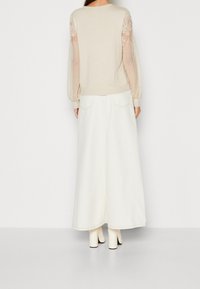 Beżowy sweter z przezroczystymi, haftowanymi rękawami, zestawiony z białą, denimową spódnicą maxi. Strój ma luźny krój i prążkowane wykończenia.