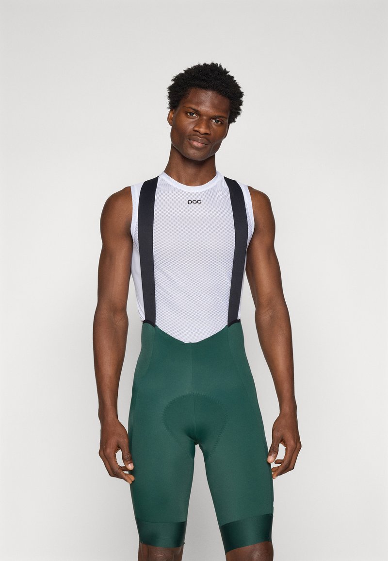 Fietsoutfit met een witte mesh top en donkergroene bretelshort. De shorts hebben een gevoerde zitting, verstelbare schouderbanden en een strakke afwerking.