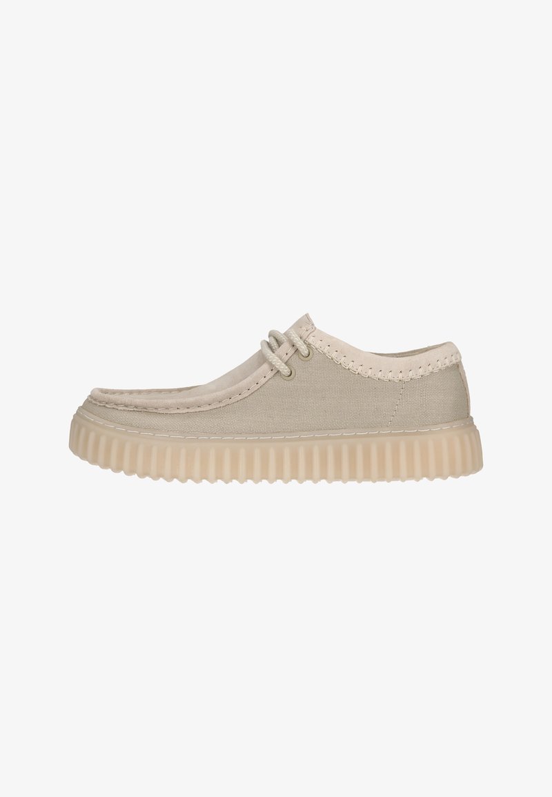 Zapato de lona color beige claro con puntera redonda, detalles de cordones y una suela de goma texturizada. Los acentos incluyen costuras a lo largo de los bordes.