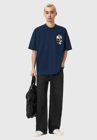 Granatowy bawełniany t-shirt z graficznym wzorem czaszki na piersi, zestawiony z luźnymi czarnymi dżinsami i białymi trampkami.