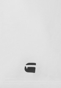 Nahaufnahme eines weißen Stoffs mit einem kleinen schwarzen stilisierten "G"-Logo in der Nähe der unteren Kante.