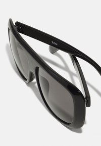 Black sunglasses with a glossy finish, wraparound style, dark lenses, and curved temple arms featuring ZIGN branding.