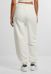 Hvide bomulds-sweatpants med elastik i taljen og ved anklerne, med en afslappet pasform. Kombineret med sorte og hvide sneakers med markeret branding.