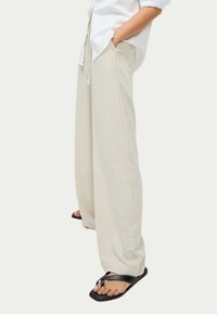Brede beige broek van lichtgewicht linnen, met een trekkoord in de taille en zakken, gecombineerd met zwarte slippers.