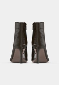 Brune krokodillemønstrede ankelstøvler med spiss tå, slank silhuett, høy stilettohæl og sølvglidelåsdetalj på baksiden.