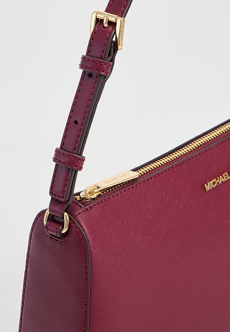 Borsa in pelle bordeaux con superficie texture, cerniera dorata e tracolla regolabile. Presenta una placca con logo e un design pulito e geometrico.