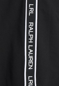 Svart tyg med en vertikal vit rand och texten "LRL RALPH LAUREN". Materialet har en slät yta och en kontrasterande textur.