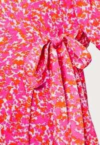 Vestido multicolorido com um padrão abstrato em rosa, laranja e branco. Apresenta um cinto amarrado na cintura e uma textura suave e macia.