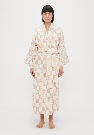 Peignoir blanc et beige à motifs avec une taille à nouer, des manches larges et une texture douce. Présente un design géométrique sur l'ensemble.