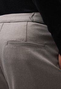 Pantalons gris sur mesure, présentant une texture lisse, un design épuré et des détails de poche arrière, avec une taille visible et des passants de ceinture.