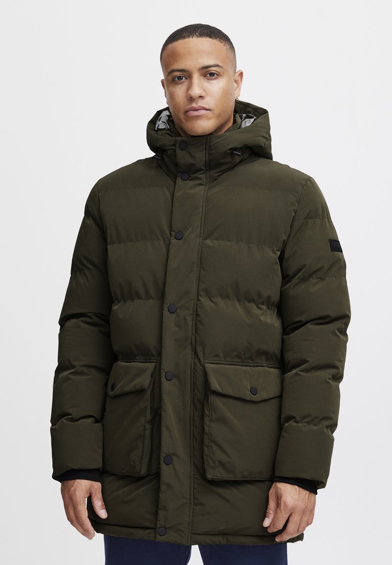Oliivroheline puffer-jakk kapuutsiga, millel on suured eespool olevad taskud, nupuga kinnitused ja must detail varrukal. Sile tekstuur.
