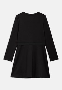 Czarna suknia z długim rękawem o gładkiej fakturze. Posiada okrągły dekolt, dopasowaną górę i rozkloszowaną spódnicę. Prosty fason bez wzorów.