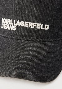 Melnā džinsa cepure ar baltu izšūtu "KARL LAGERFELD JEANS" logotipu priekšējā panelī.