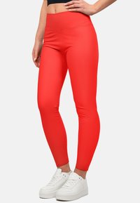 Rode high-waisted leggings gemaakt van rekbare, gladde stof, gecombineerd met witte sneakers. Kenmerkt een slank, passend ontwerp.