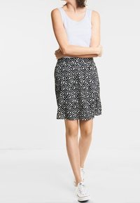 Černobílá vzorovaná sukně s geometrickým designem. Volná látka, délka po kolena, kombinováno s bílým tílkem a bílými teniskami.