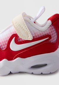 Dječja crveno-bijela Nike tenisica sa čičak trakom, bijelim swoosh logotipom, mrežastim gornjim dijelom i mekanim potplatom s vidljivom zračnom jedinicom.
