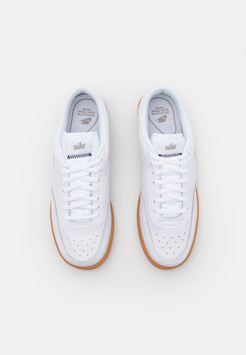 Białe sneakersy Nike z gładką skórzaną cholewką, perforowanym noskiem, płaskimi sznurówkami i gumową podeszwą. Teksturowane detale na bokach.