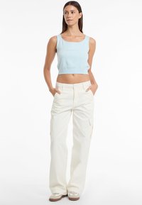 Top corto di colore blu chiaro, in maglia di cotone, con scollo tondo; abbinato a pantaloni cargo bianchi con tasche laterali e taglio dritto.
