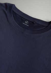 Mornarsko modra bombažna majica s krožno ovratnikom, gladko teksturo in stranskim oznako blagovne znamke. Klasičen kroj, brez vidnih vzorcev ali poudarkov.