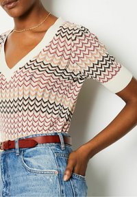 Knitted short-sleeve top featuring a chevron pattern in shades of cream, brown, and red. V-neck design with a textured finish.
