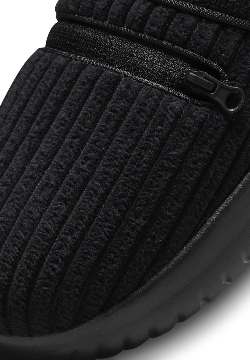 Zapatillas negras con textura acanalada, cierre de cremallera y suela texturizada. Fabricadas con un material suave y aterciopelado.