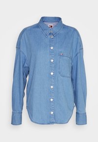 Camicia di jeans azzurro chiaro con maniche lunghe, chiusura a bottoni, colletto classico, taschino sul petto e discreto dettaglio del logo sulla tasca.