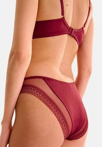 Ensemble de lingerie bordeaux comprenant un soutien-gorge en tissu doux avec des bretelles réglables et un slip assorti avec des détails en dentelle et en mesh transparent.