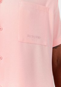 Kortärmad rosa skjorta med texturerad tyg, med en bröstficka och diskret varumärke "SIXTHJUNE PARIS" broderat i samma färg.