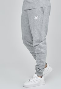 Gray sweatpants with a relaxed fit, featuring pockets and a white logo accent. Paired with white sneakers for casual wear.