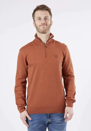 Pull à col zippé couleur rouille avec des poignets et un ourlet côtelés, fabriqué à partir d'un matériau doux. Présente un petit logo sur la poitrine.