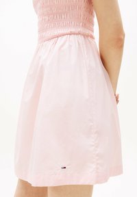 Vestido rosa con cuerpo fruncido y falda acampanada. Hecho de una tela ligera, cuenta con un pequeño parche de logo cerca del dobladillo.