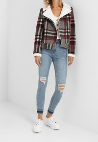 Skotskjakke med hvid fleecekrave, parret med lyseblå ripped skinny jeans og hvide sneakers. Jakken har lynlås og knapper.