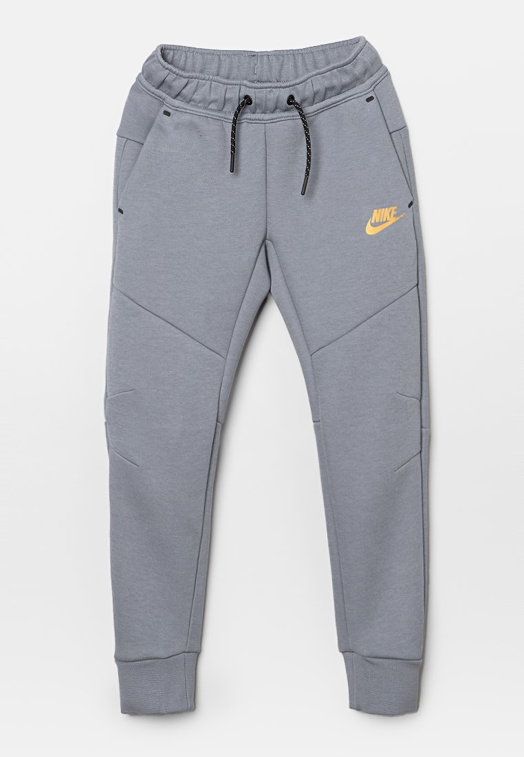 Pantaloni sportivi grigi con vita elasticizzata, cordoncino e tasche laterali. Presentano il logo Nike arancione, un tessuto testurizzato e un design con gamba affusolata.