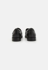 Chaussures habillées en cuir noir avec un fini lisse, présentant un bout arrondi et des coutures décoratives sur le talon et les côtés. Semelle plate.