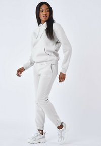 Sudadera gris claro y pantalones de chándal a juego, con un acabado texturizado, puños elásticos y un bolsillo frontal. Zapatillas con acentos grises.
