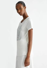 T-shirt bianco a maniche corte con una grafica quadrata testurizzata in argento. Tessuto di cotone morbido con un taglio rilassato e scollo rotondo.
