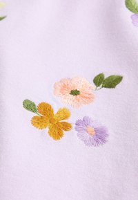 Tejido bordado con flores moradas, melocotón y amarillas sobre un suave fondo lavanda, con hojas verdes y un detallado bordado.