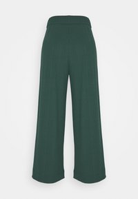 Tummanvihreät leveät ribbikudoslahkeet, joissa on korkea joustava vyötärö ja huomaamaton pystysuora tekstuuri yksinkertaisella taustalla.