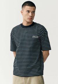 Marinblå stribet T-shirt med hvide horisontale linjer, ribbet rund hals og broderet "COPENHAGEN" accent på brystet. Korte ærmer.