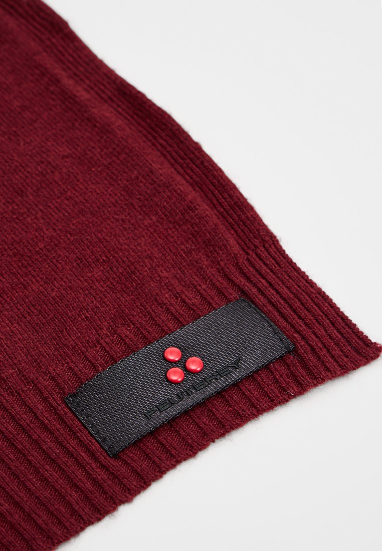 Burgunderfarbener Wollstoff mit einem schwarzen Etikett, das drei rote Punkte und den Markennamen zeigt. Der Stoff hat eine gerippte Textur.