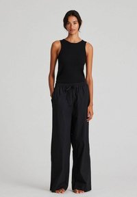 Black ribbed tank top paired with loose-fitting black trousers. The outfit features a simple, minimalistic design and a relaxed fit.