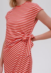Robe rayée rouge et blanche à manches courtes, dotée d'un détail de lien sur le côté. Tissu lisse avec une silhouette ajustée.