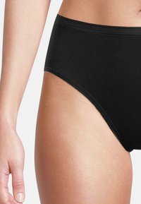 Schwarze hochgeschnittene Slips aus dehnbarem Material mit glatter Oberfläche, die über dezente Bundnähte und einen klassischen Schnitt verfügen.
