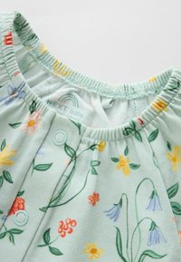 Vêtement bébé vert menthe doux avec encolure élastique, boutons pression et imprimé floral coloré incluant des fleurs jaunes, rouges et violettes.