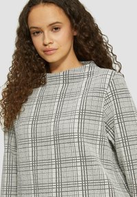 Grau-weißer, gemusterter Pullover mit hohem Kragen, aus strukturiertem Stoff und in kastiger Silhouette. Auffälliges Rautendesign über das gesamte Kleidungsstück.