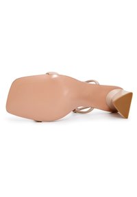Beige korkokenkä, jossa on kolmio muotoinen tan korko, sileä pinta, avonainen takakappale ja ohuet hihnat. Pohjassa on vaakasuorat pitoa helpottavat urat.