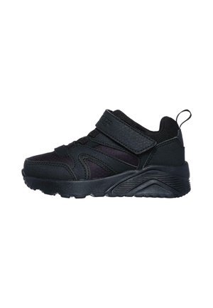 Zapatilla deportiva negra con tira de velcro, suela texturizada y cinta para tirar en el talón, diseñada para la comodidad y fácil cierre.