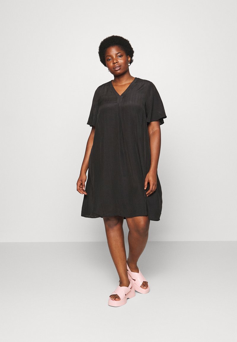 Vestido preto de mangas curtas com decote em V, silhueta fluida e textura suave, combinado com sandálias de plataforma em rosa claro.